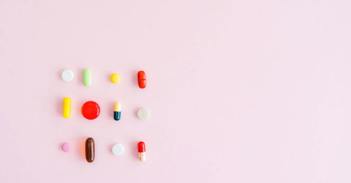 Colorido surtido de pastillas y cápsulas dispuestas sobre un fondo rosa pastel, perfecto para temas de salud.