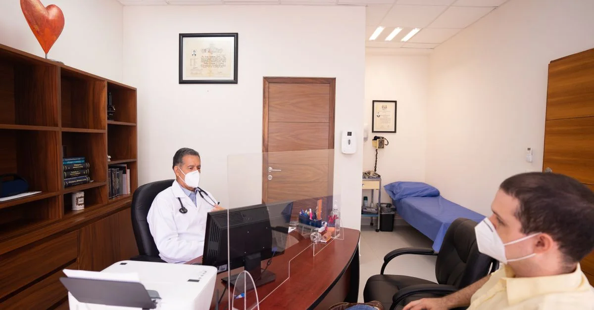 Médico y paciente con mascarillas en clínica médica, enfatizando la seguridad en la atención médica.