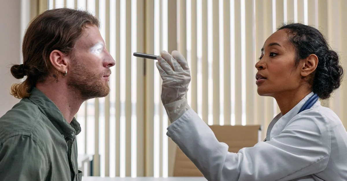 Un médico realiza un examen ocular a un paciente utilizando una linterna en un entorno clínico.
