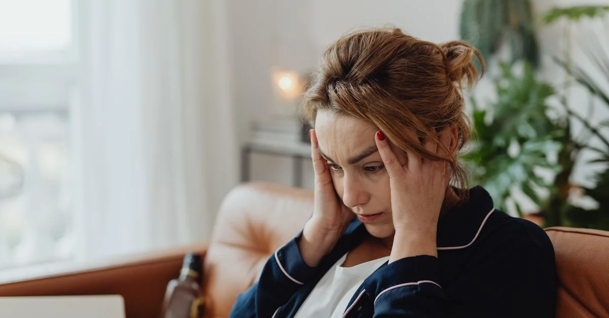 Una mujer en pijama se sienta en interiores con las manos en la cabeza, mostrando estrés y frustración. Perfecto para temas de salud mental.