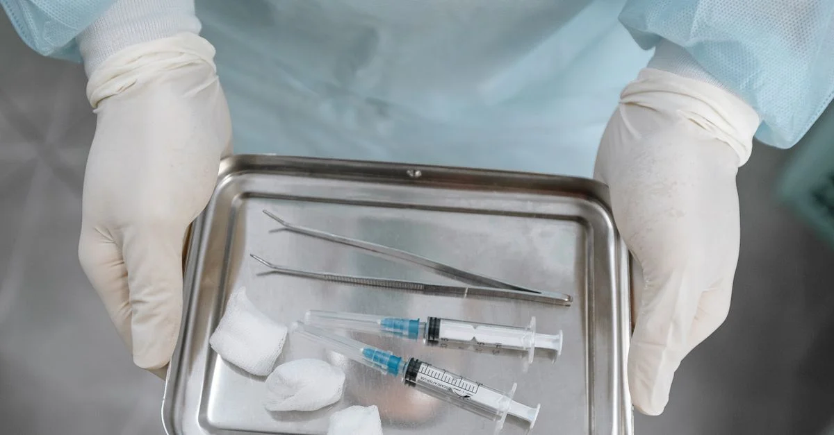 Primer plano de un profesional médico con jeringas, pinzas y gasa en una bandeja de acero.