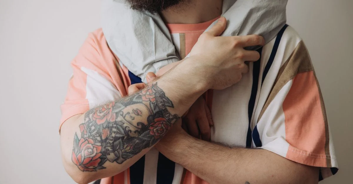 Primer plano de un hombre tatuado con una camiseta estampada abrazando con un toque personal.