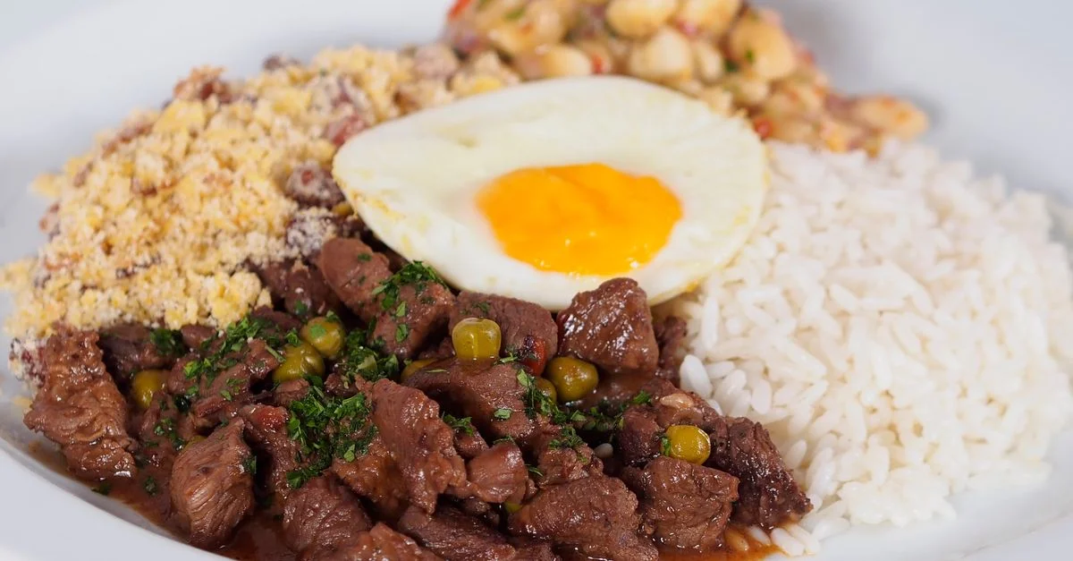 Un plato de feijoada brasileña con arroz, frijoles, farofa y un huevo frito.