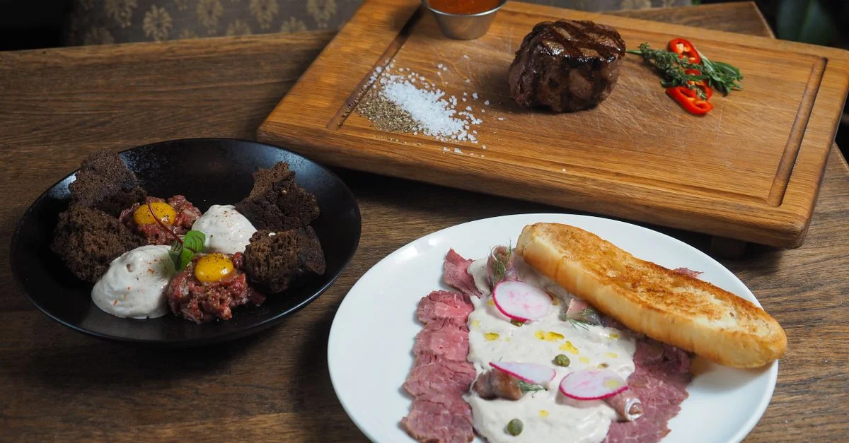 Deliciosos platos gourmet de carne con bistec, tartar de carne y salsas sazonadas en una mesa rústica de madera.