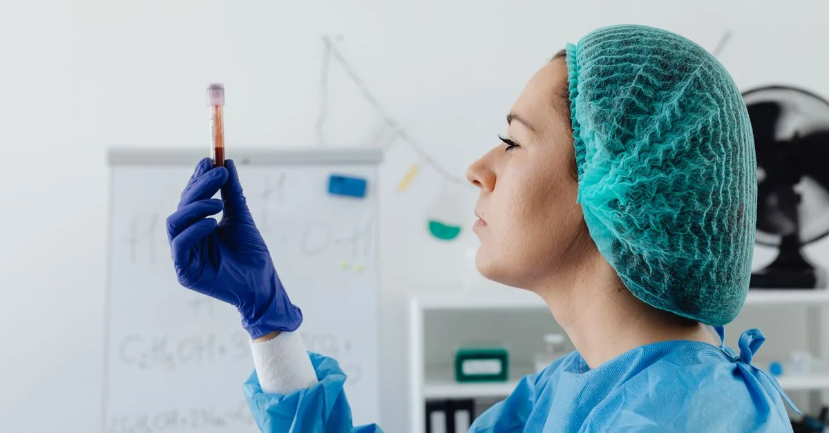 Una científica en equipo de protección inspecciona un vial de muestra de sangre en un entorno de laboratorio.
