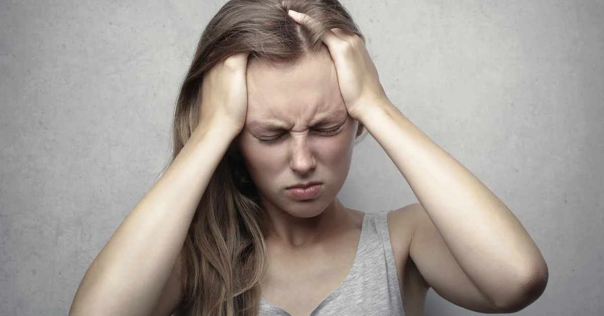 Joven mujer expresando estrés y frustración mientras se agarra la cabeza.